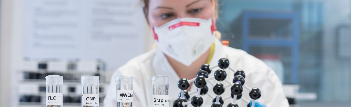 Student in protective mask looking at graphene and test tubes